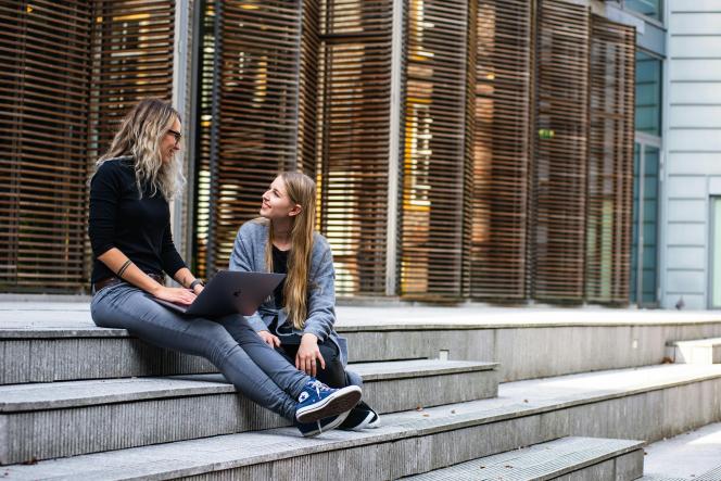 zwei Frauen sitzen mit einem Laptop vor einem Universitätsgebäude